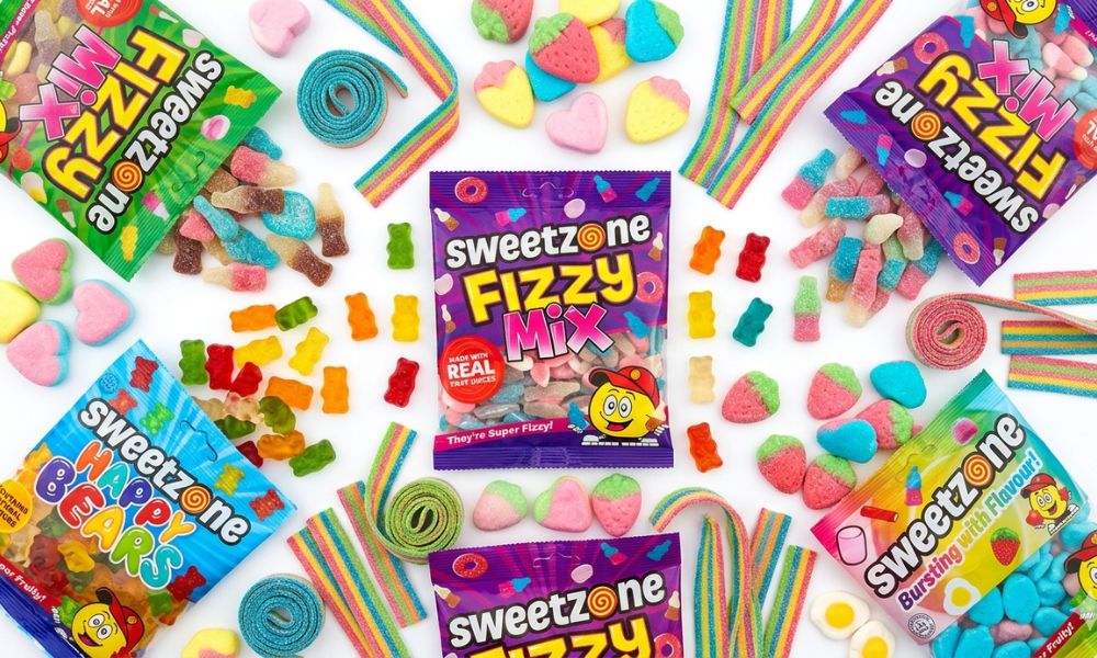 A colourful spread of Sweetzone branded sweets including gummies, fizzy belts and foam sweets on a white surface