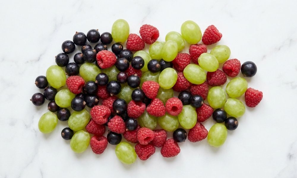 Fresh blackcurrants, raspberries and grapes arranged together on a white surface